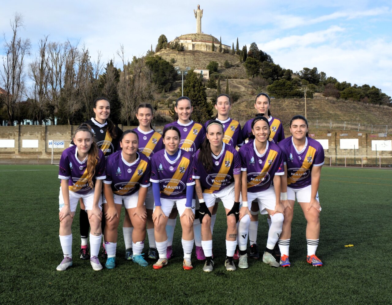 Equipo de fútbol femenino de Palencia posando en el campo con un monumento al fondo.