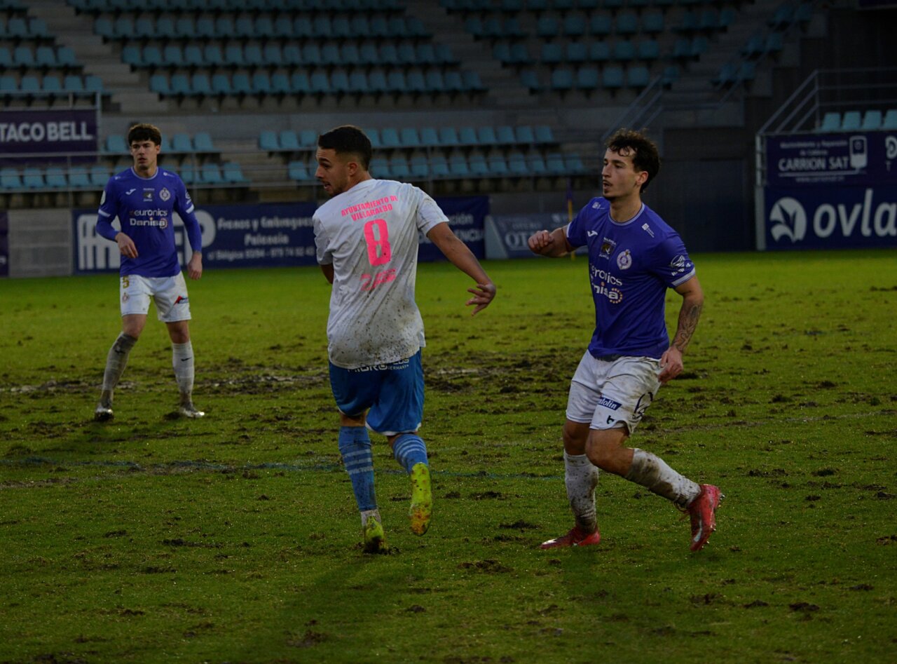 Jugadores de fútbol en un campo con césped en mal estado durante un partido en Palencia