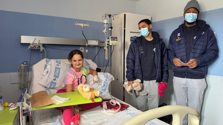 Jugadores de baloncesto visitan a una niña en el hospital con peluches.