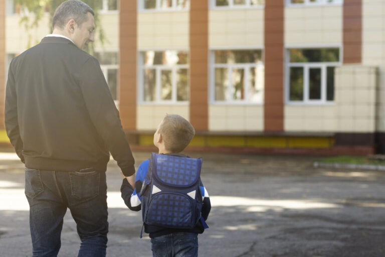 Padre y niño caminando hacia la escuela en su primer día escolar