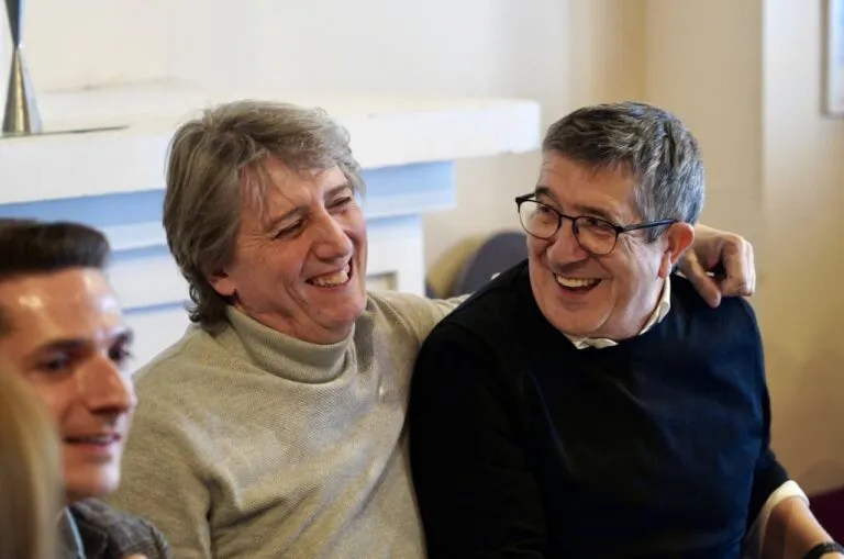 Dos hombres sonriendo en un ambiente amigable durante un evento político.