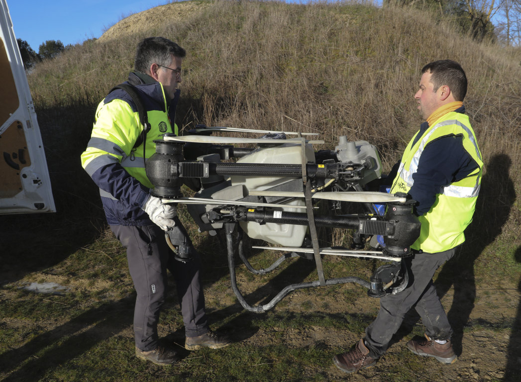 Dos hombres transportando un dron agrícola en un terreno rural