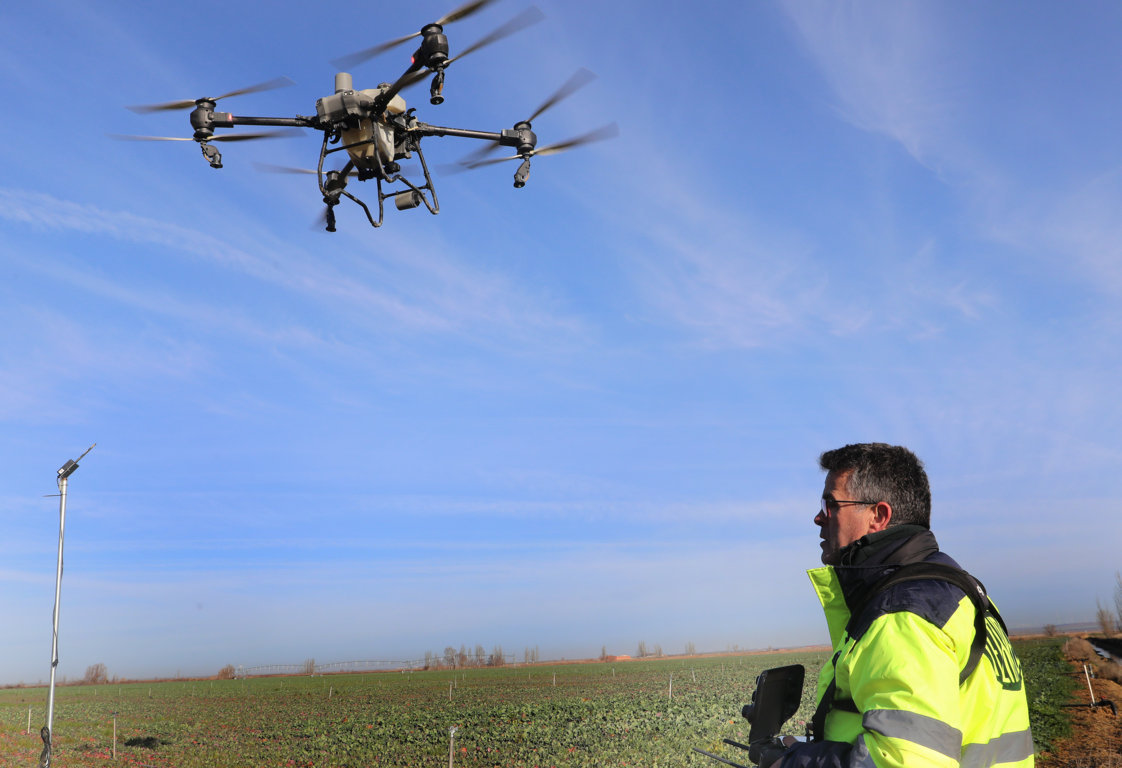 Dron volando sobre un campo agrícola con un operador observando