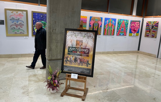 Exposición de arte con cartel de Bollywood y pinturas coloridas en la biblioteca.