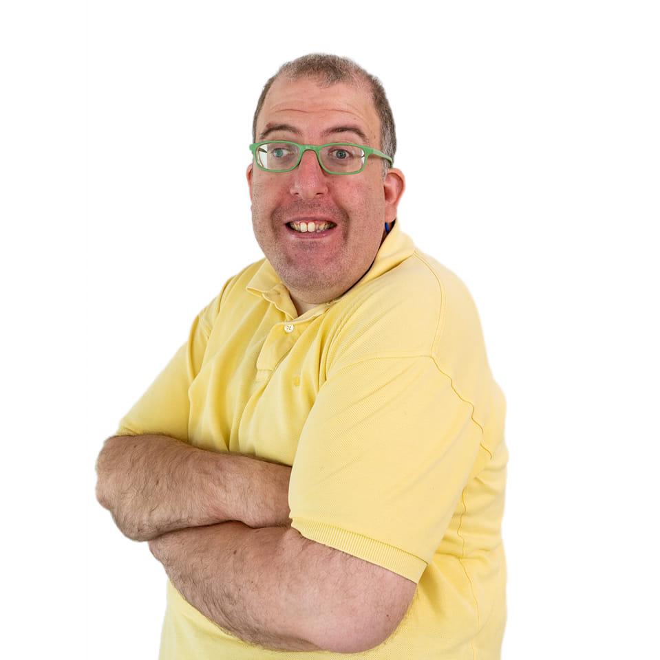Actor sonriente con camiseta amarilla y gafas verdes en un fondo blanco