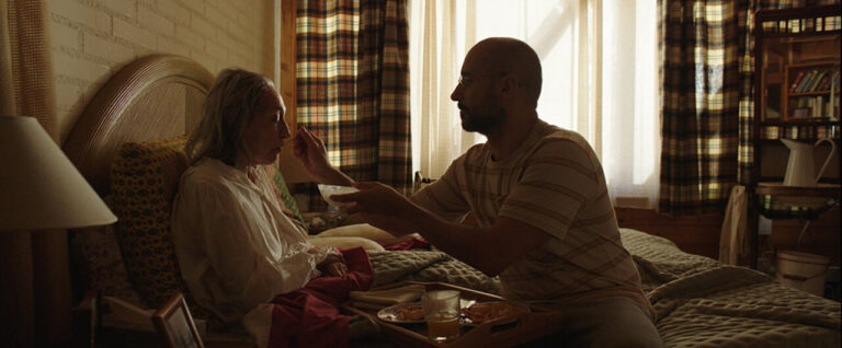 Hombre alimentando a una mujer mayor en una habitación iluminada.