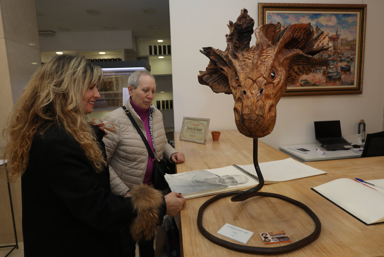 Escultor mostrando una obra de arte en madera en una exposición