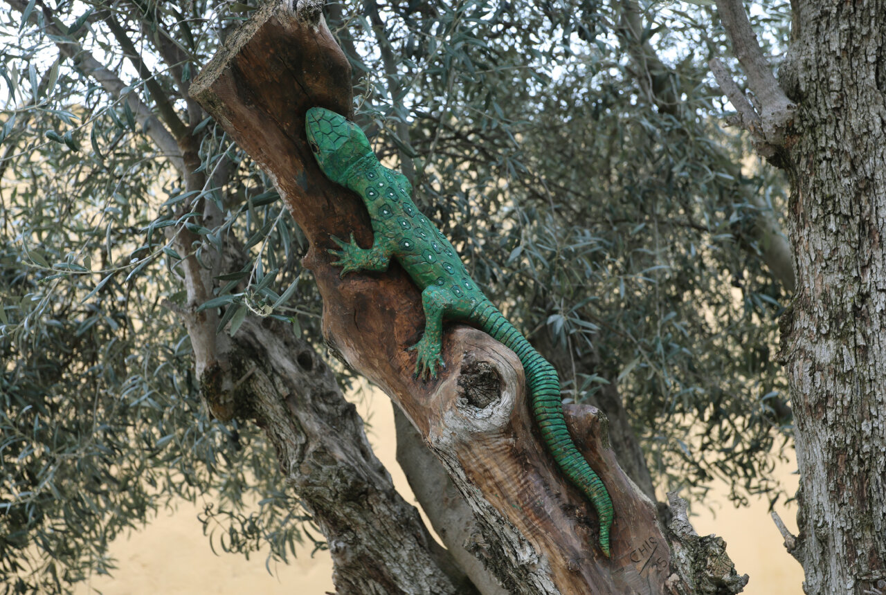 Escultura de un lagarto verde tallado en madera sobre un tronco