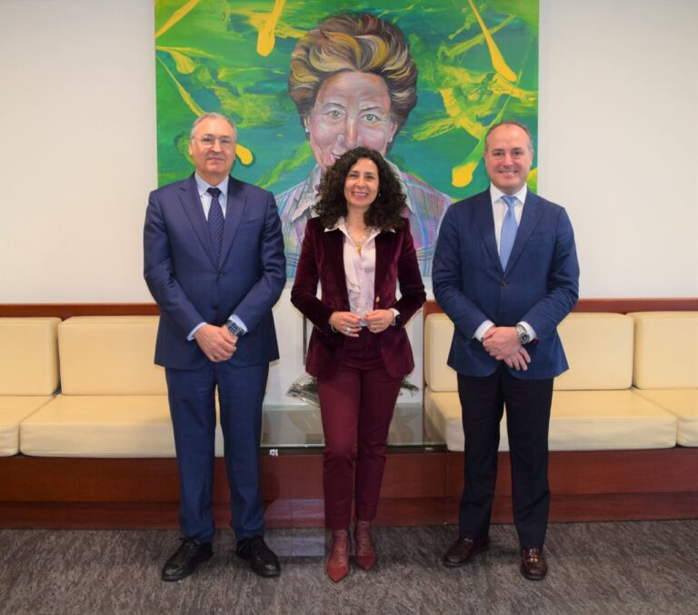 Tres personas posando en una oficina con un retrato colorido de fondo
