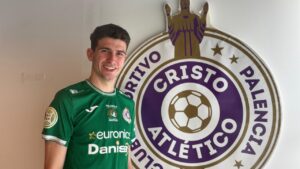 Javi García, guardameta del Palencia Cristo Atlético, sonríe junto al escudo del club.