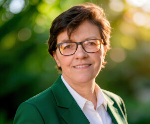 Retrato de una mujer con chaqueta verde y camisa blanca en un entorno natural.