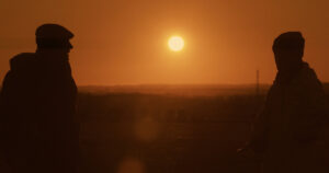 Dos personas en silueta con un atardecer de fondo en un campo