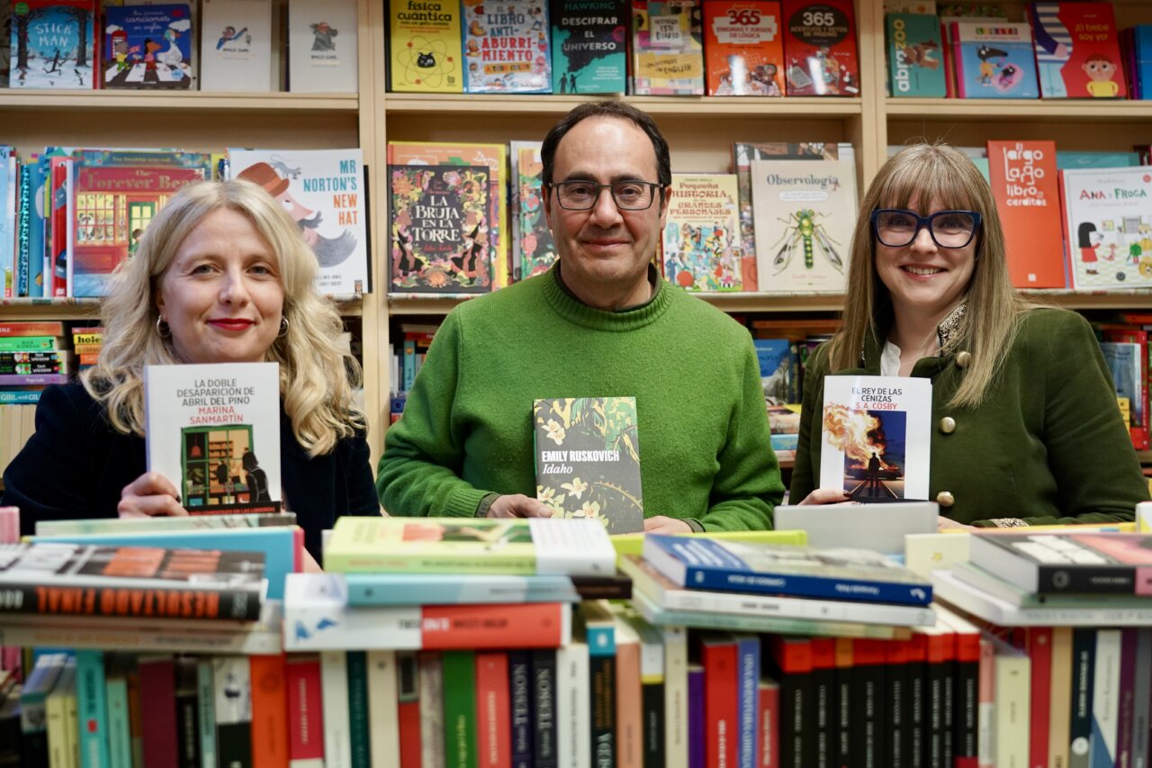Tres personas sosteniendo libros en una biblioteca con estanterías llenas