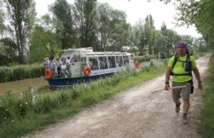 Turistas navegando en el Canal de Castilla mientras un senderista camina por el camino