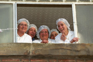 Grupo de mujeres galleteras sonriendo desde una ventana de la fábrica
