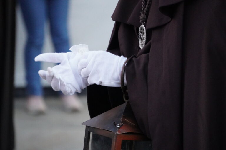 Mano con guantes blancos sosteniendo una linterna en una procesión religiosa