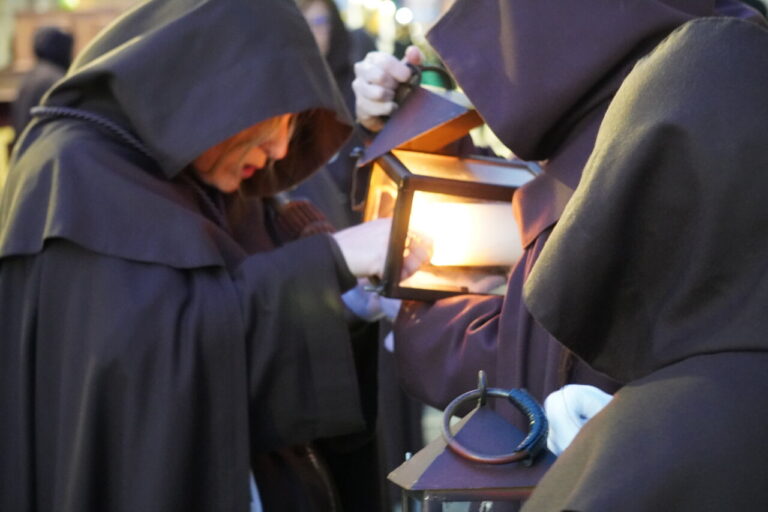 Cofrades con túnicas oscuras sosteniendo faroles en la procesión