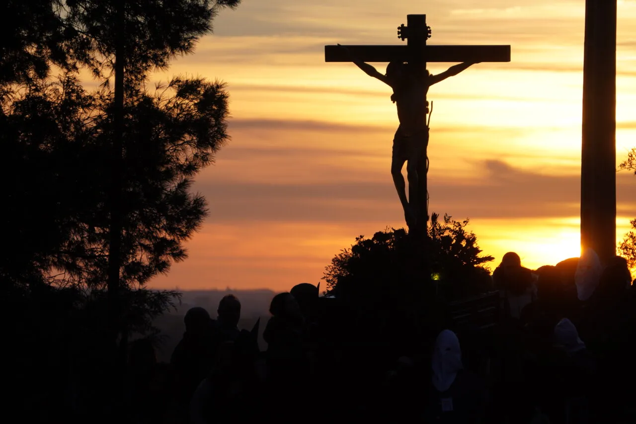 Silhouette of a crucifix during a procession at sunset.