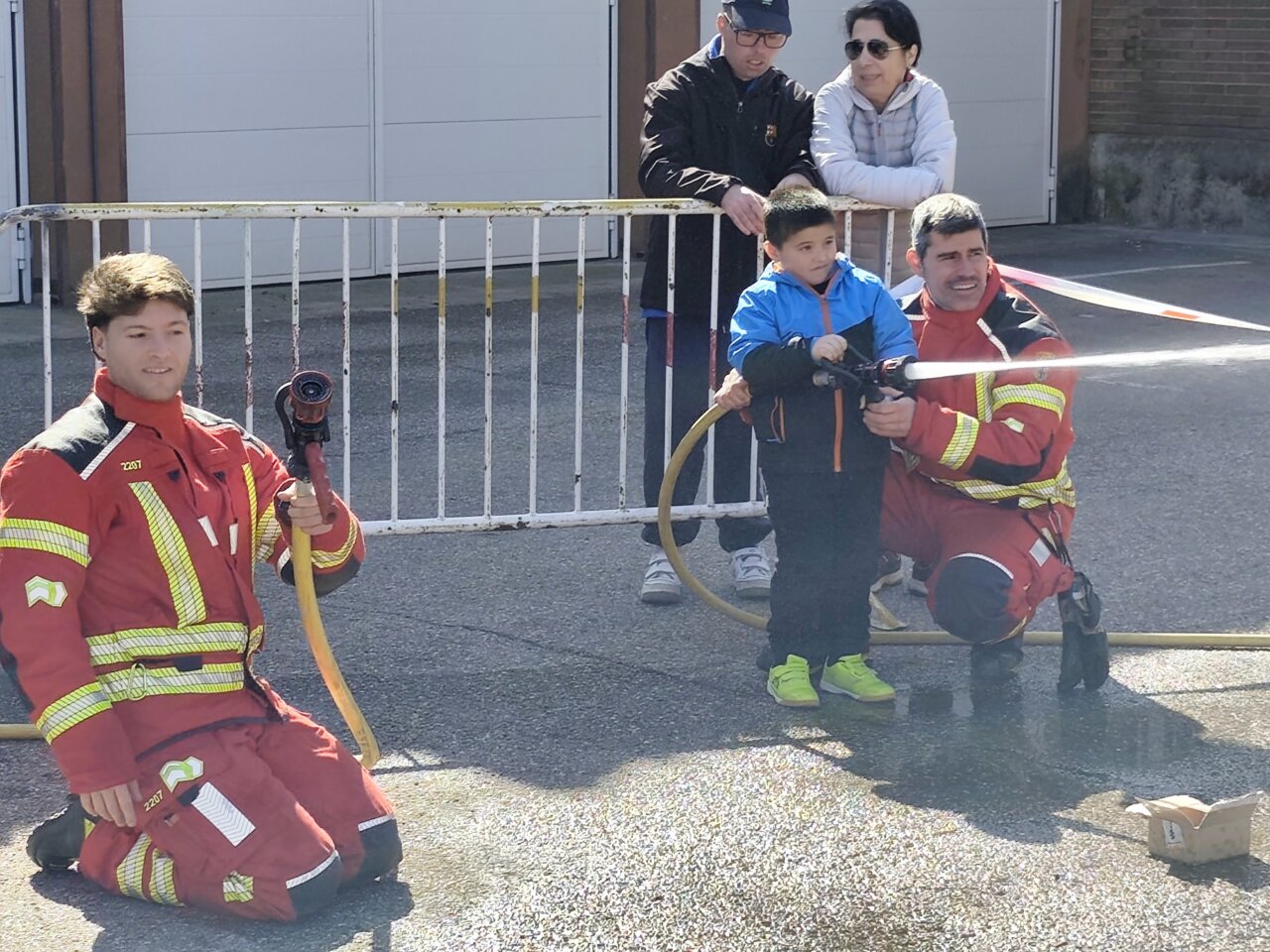Niño y bomberos usando una manguera en una jornada de puertas abiertas