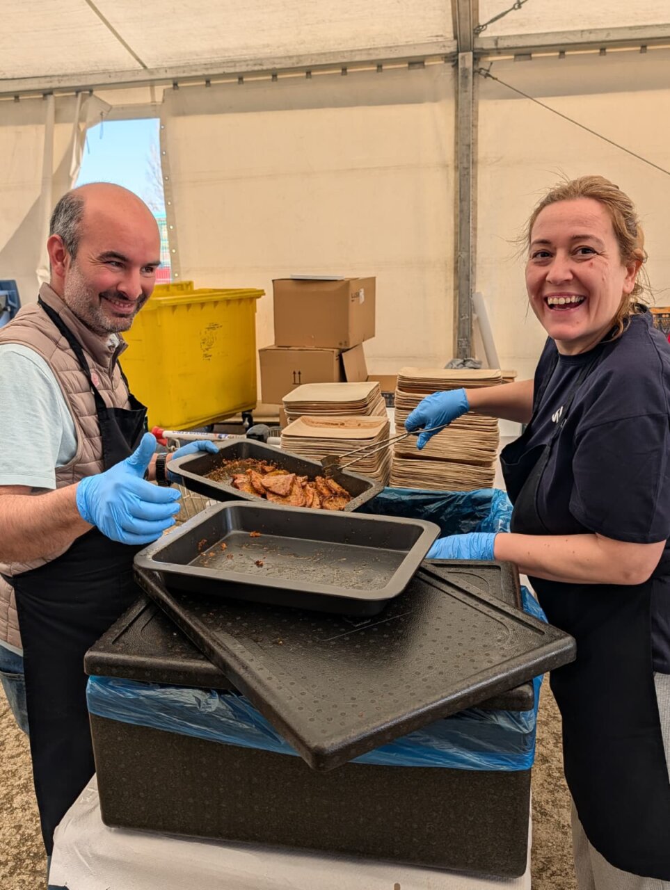 Dos personas sonrientes preparando comida en la Feria de la Matanza en Villada.