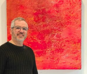 Alberto Reguera posando frente a una obra de arte abstracto roja
