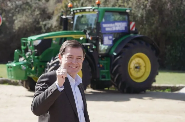 Candidato del PP sonriendo frente a un tractor John Deere en campaña electoral.