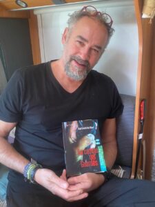 Carmelo Ruiz sosteniendo su novela La cadena del guardés en un entorno acogedor.