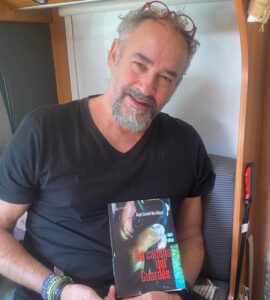 Carmelo Ruiz sosteniendo su novela La cadena del guardés en un entorno acogedor.