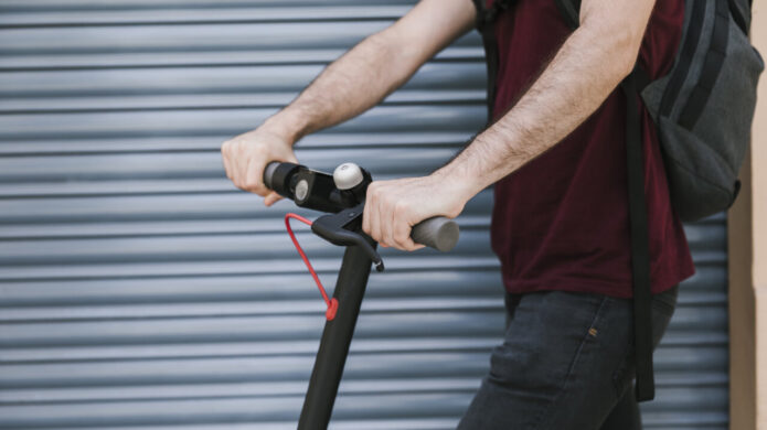 Conductor de patinete eléctrico en la calle con fondo gris