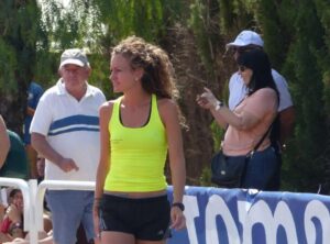 Elena Caballero en un evento de atletismo, con camiseta amarilla y cabello rizado