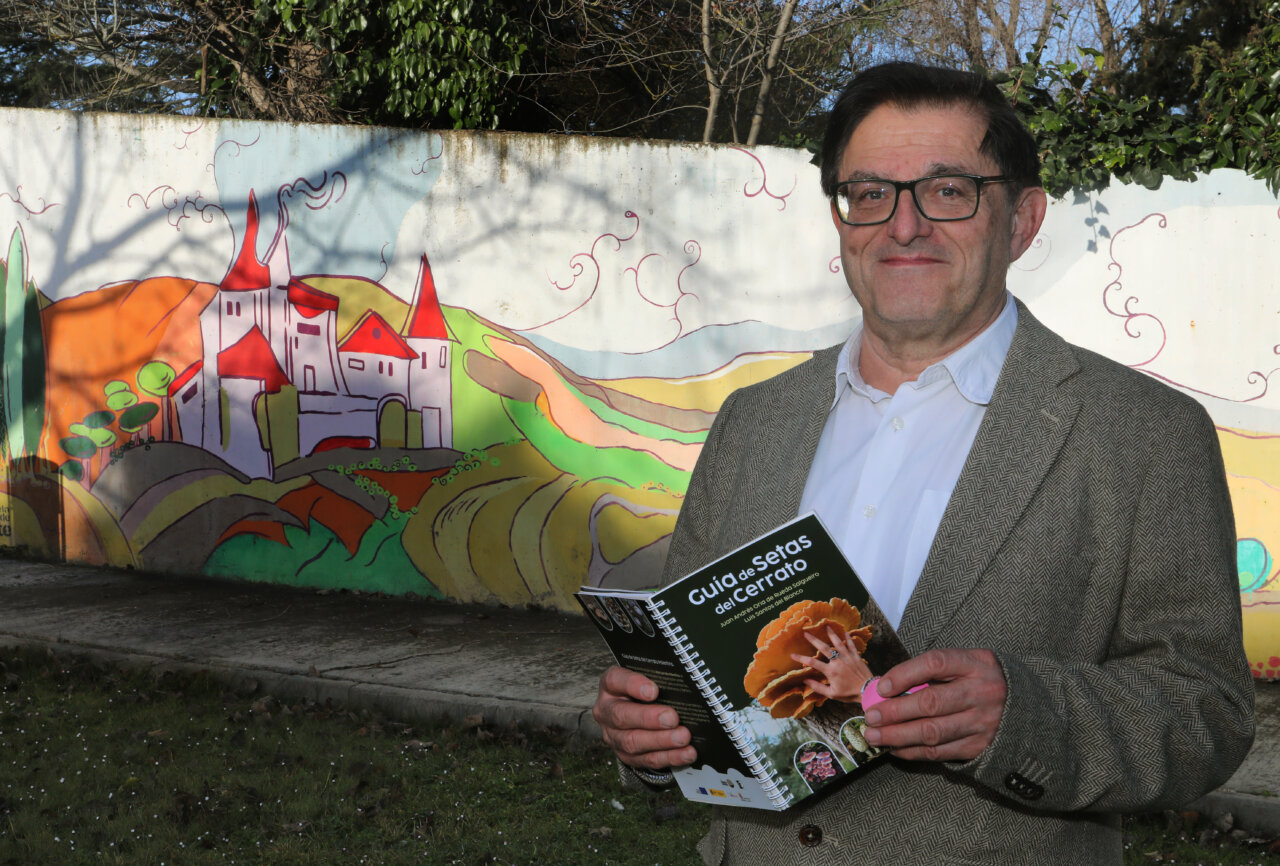 Hombre sosteniendo la guía de setas del Cerrato Palentino frente a un mural colorido.