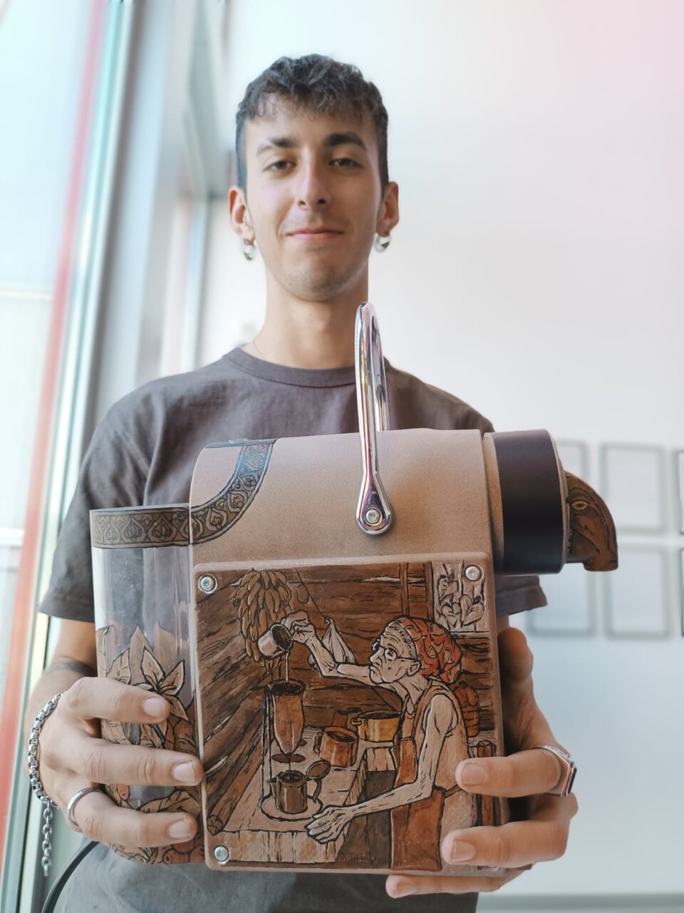 Joven artista sosteniendo una cafetera decorada en un evento cultural.