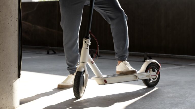 Joven de pie junto a su patinete eléctrico en un aparcamiento