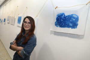 Artista junto a obras de cianotipia en exposición sobre lavaderos