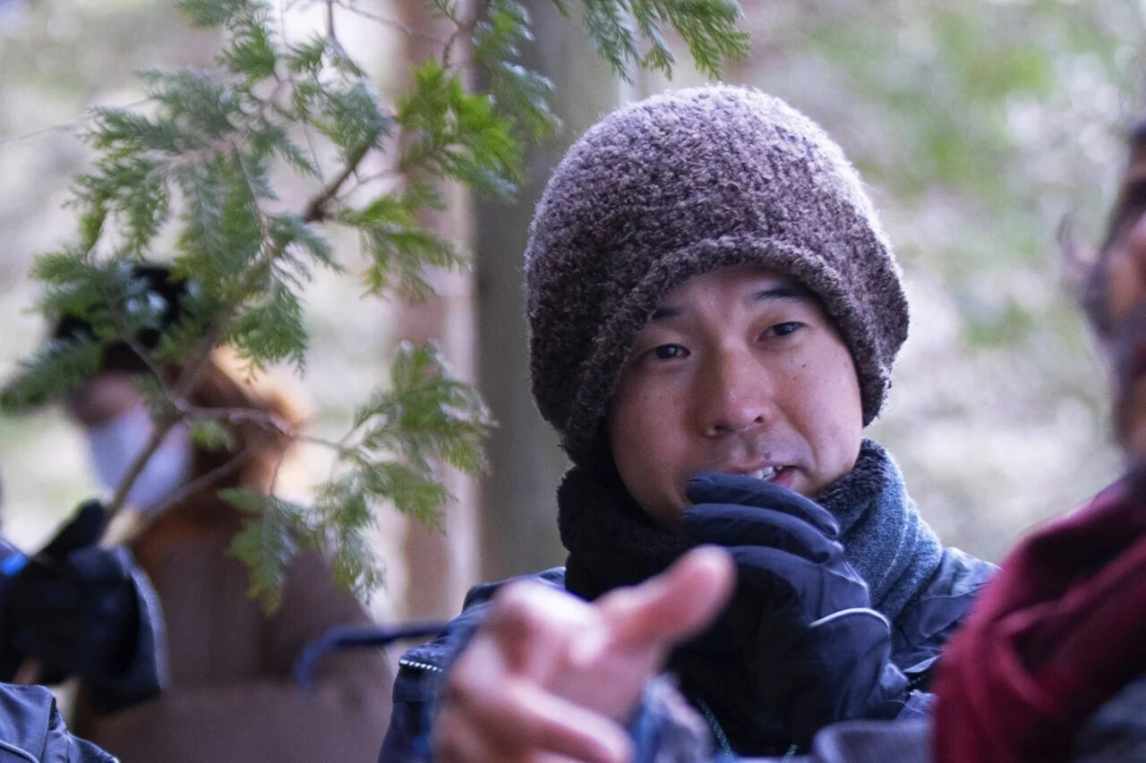 Masakazu Kaneko en un entorno natural, vestido con abrigo y gorro.