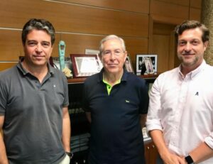 Tres hombres posando en un entorno de oficina con trofeos y fotos