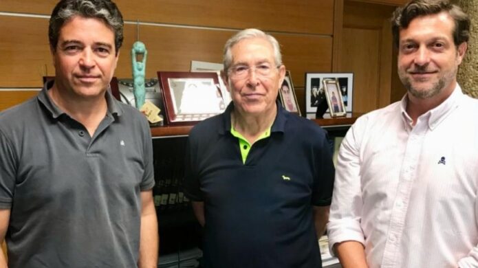 Tres hombres posando en un entorno de oficina con trofeos y fotos
