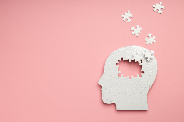 Cabeza de rompecabezas blanca sobre fondo rosa simbolizando salud mental