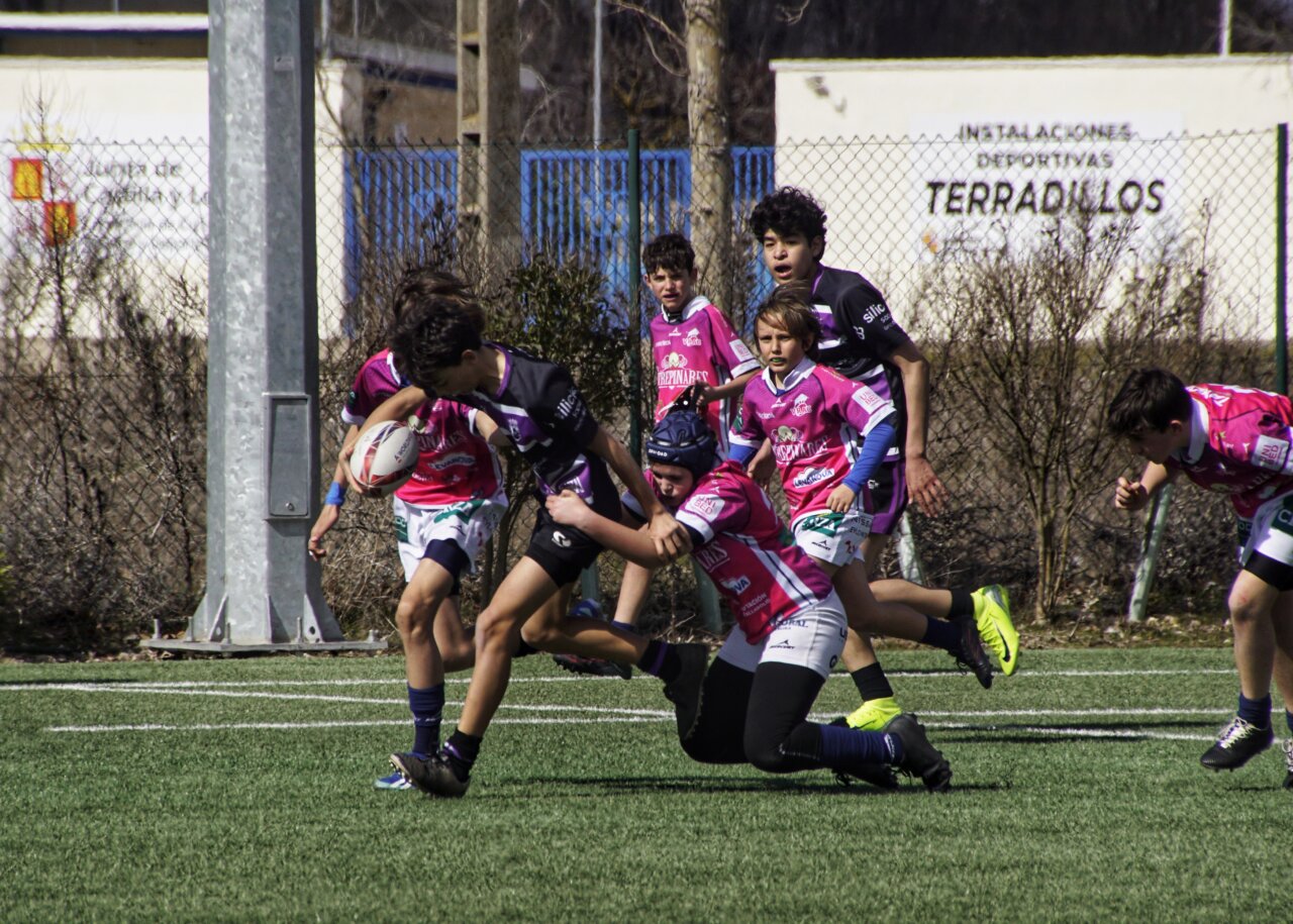 Un jugador sub-14 de rugby intenta avanzar mientras es placado por un rival.