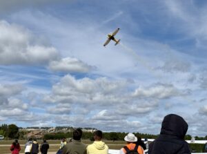 Un avión realizando acrobacias aéreas en un aeródromo con espectadores