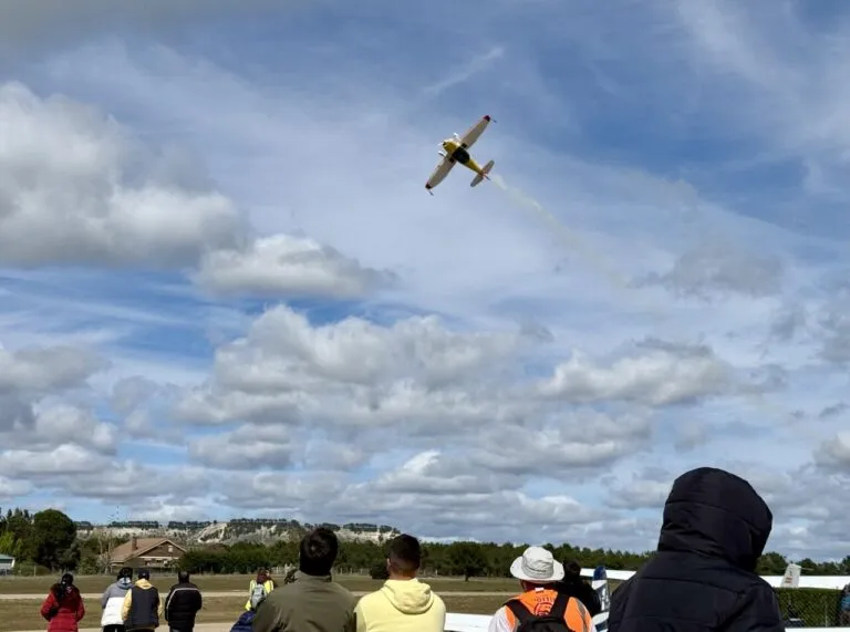 Un avión realizando acrobacias aéreas en un aeródromo con espectadores