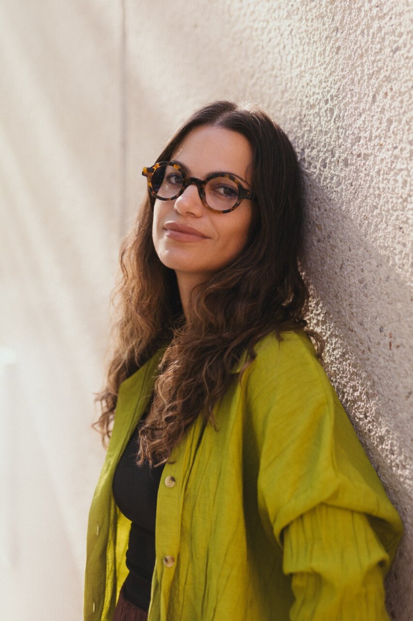 Retrato de Laura Sanz con camisa verde y gafas, sonriendo.