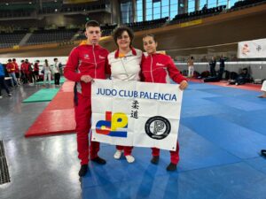 Tres miembros del Judo Club Palencia sosteniendo una pancarta en un campeonato