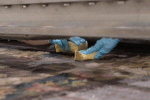 Manos con guantes limpiando un tapiz con esponjas