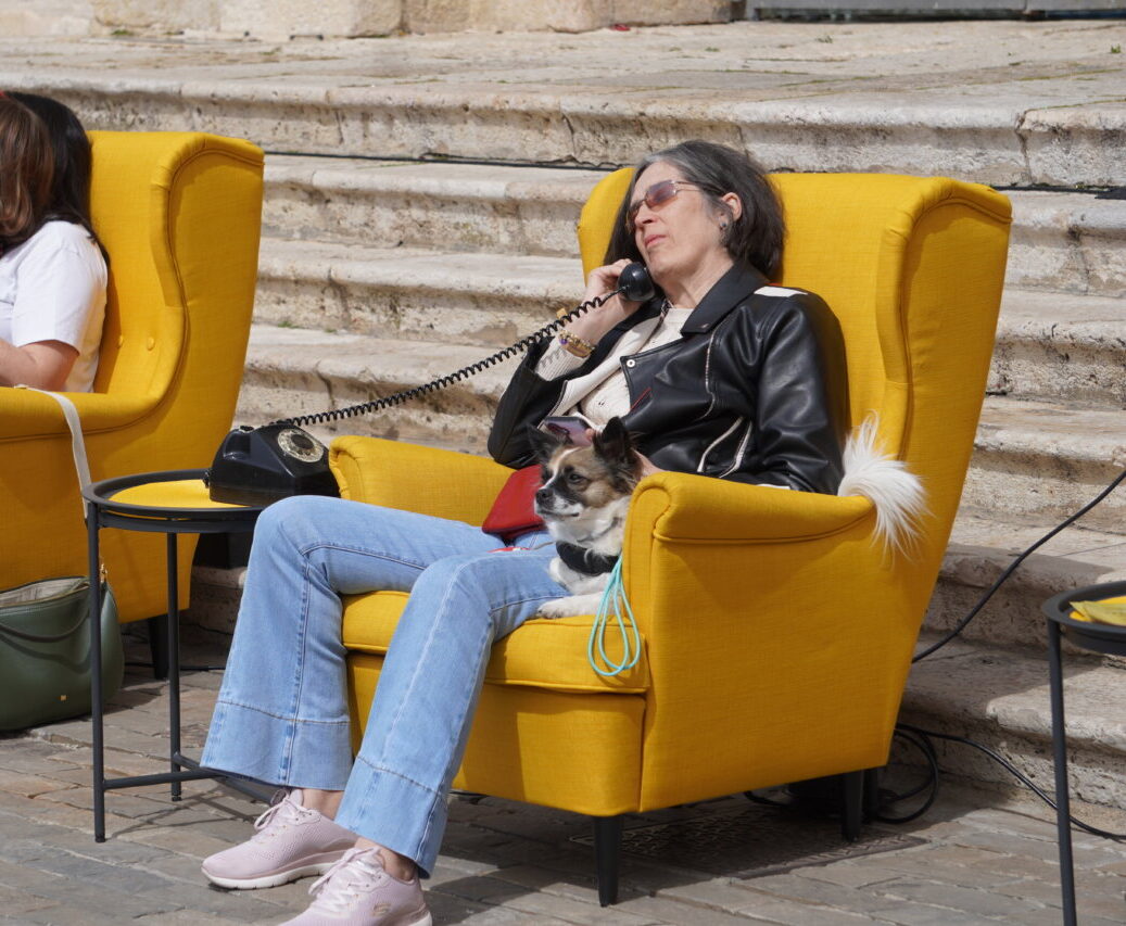 Personas sentadas en sillones amarillos usando teléfonos en la plaza