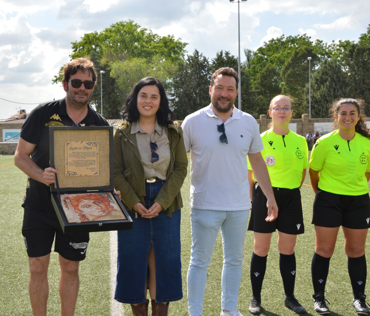 Entrega de un premio en el campo de fútbol con jugadores y árbitros presentes