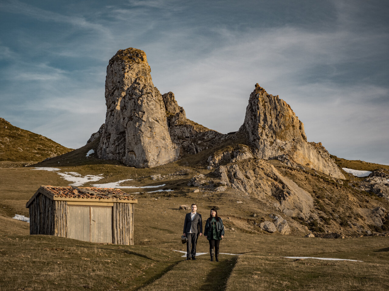 Dos personas caminando en un paisaje montañoso con formaciones rocosas
