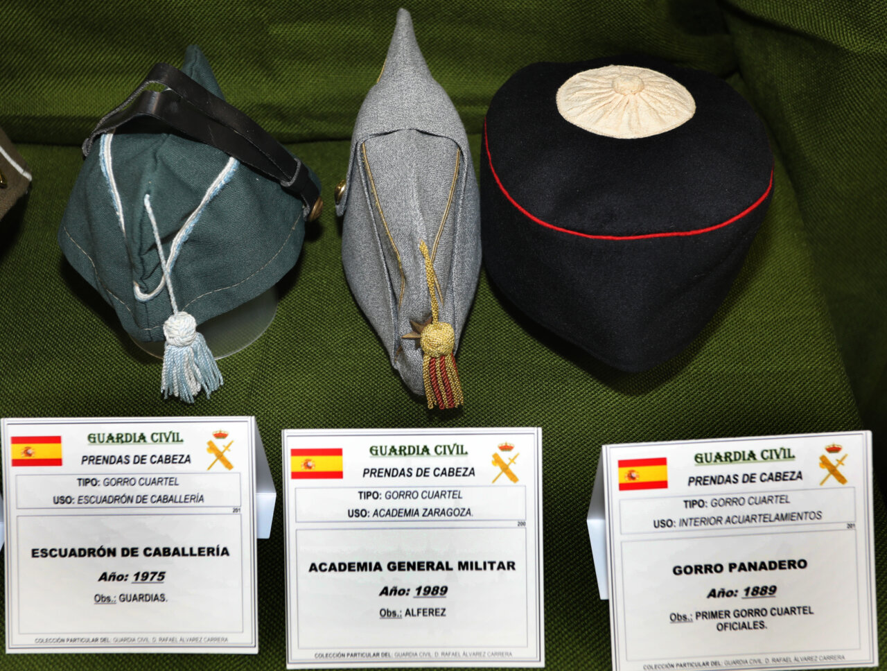 Tres gorros de la Guardia Civil en exposición con etiquetas informativas.