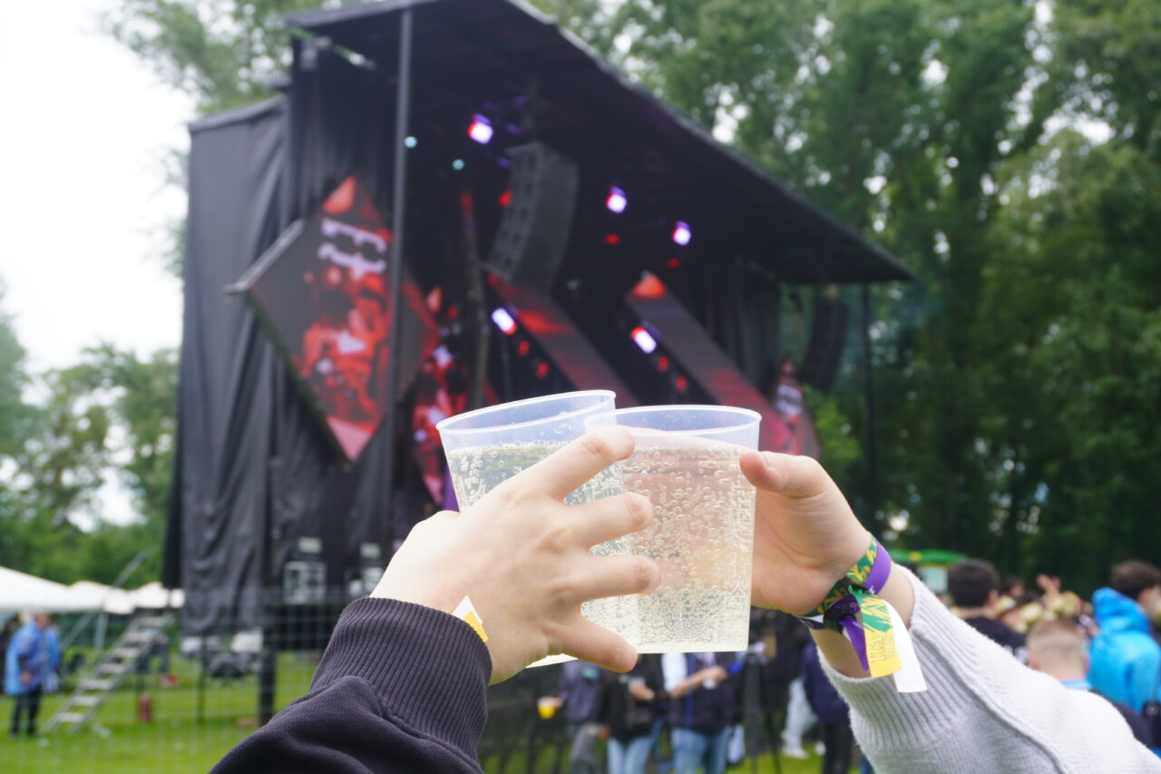 Dos manos levantando vasos en un festival bajo la lluvia
