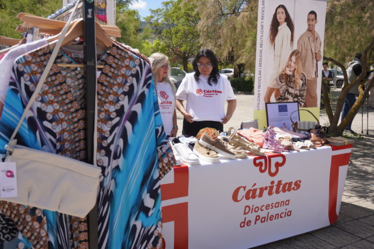 Mujeres en un stand de Cáritas mostrando ropa y accesorios en un desfile de moda sostenible.